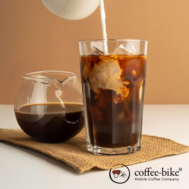 Cold Brew Kaffee in einem Glas mit eingegossener Milch, daneben eine Karaffe mit weiterem Cold Brew – erfrischendes Kaffeegetränk im Trend.