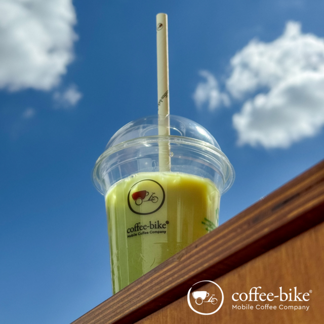 Iced Matcha Latte im Coffee-Bike Becher vor blauem Himmel
