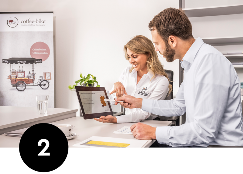 Femeie angajată în cămașă Coffee-Bike indică o tabletă cu o prezentare de vânzări cu un francizat în sala de ședințe